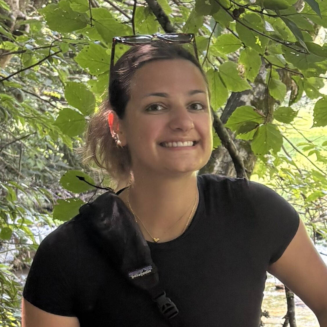 Portrait photo of grad student Liz Kelley posing in a forest with green branches of a tree behind her.